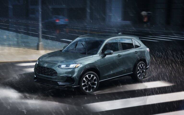 2027 Honda HR-V EX-L in Nordic Forest Pearl profile view driving on a rainy city street (Subcompact Crossover SUV).