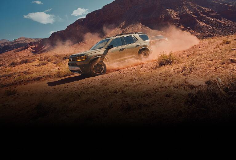 2027 Honda Passport TrailSport Elite in Ash Green Metallic profile driving on a dusty desert trail (Mid-Size SUV).